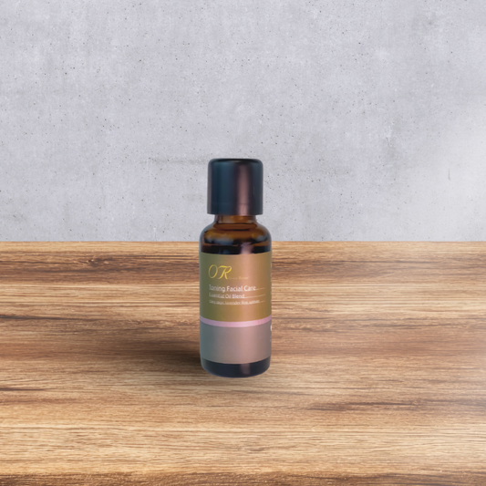 A small amber glass bottle of OR Facial Care serum with a black cap, standing on a wooden surface against a textured gray concrete wall.