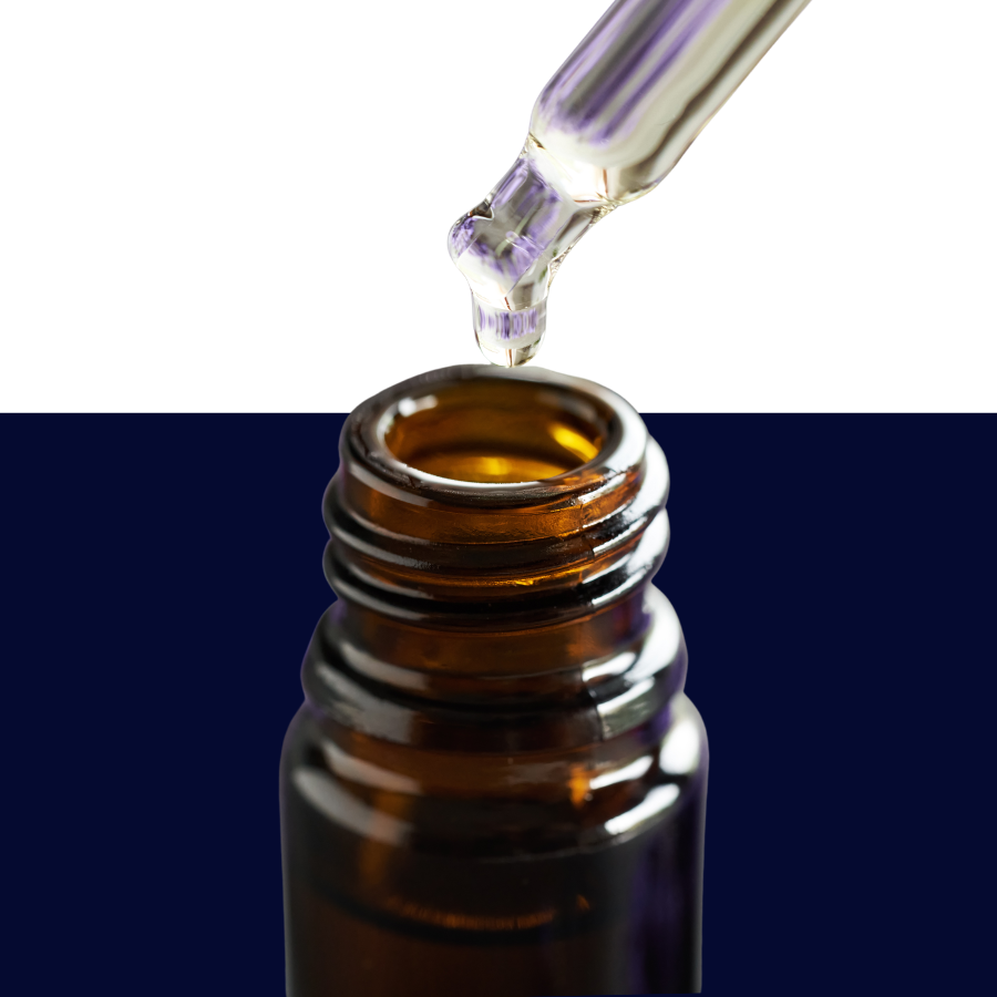 A close-up of a glass dropper above an amber brown bottle, with a clear liquid drop falling into the bottle against a split white and dark navy background.