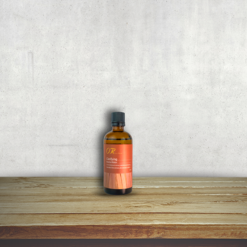 An amber glass bottle of hair growth serum with a black cap and an orange label, standing on a light wood surface against a textured light gray wall.